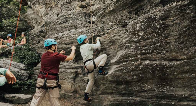 a student rock climbs while another spots them on a rock climbing trip in north carolina